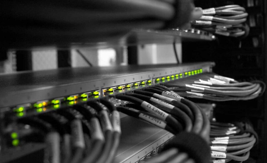 Serverschrank mit einer Reihe beleuchteter grüner LEDs an einem Switch und gebündelten Ethernet-Kabeln, die beschriftet und ordentlich in einem Serverschrank arrangiert sind