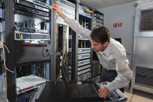 man_datacenter - A DataRoad - A DataRoad Technician in a data center reaching to rack servers, with a laptop on a rolling cart nearby and network cables in the racks.