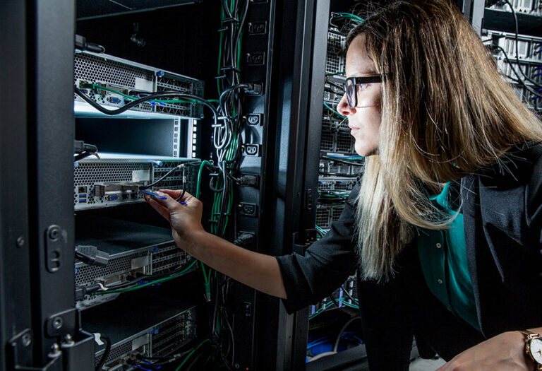 Une technicienne informatique dans un centre de données branche un câble réseau sur un serveur monté en rack.
