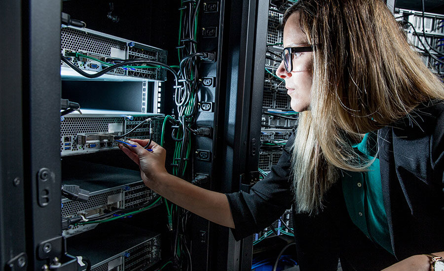 Weibliche IT-Technikerin in einem Rechenzentrum steckt ein Netzwerkabel in einen Rack-Server.