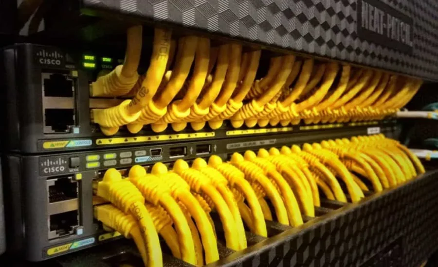 Reihe von Cisco-Netzwerkswitches mit zahlreichen angeschlossenen gelben Ethernet-Kabeln.