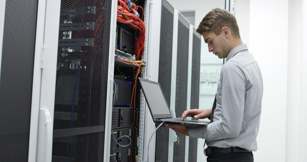 An IT technician using a laptop to configure servers in a data centre cabling room